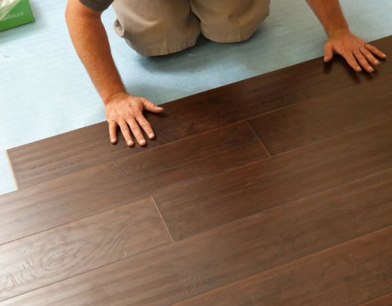 A man kneeling on a wooden floor, illustrating a flooring service based in Sacramento, CA.