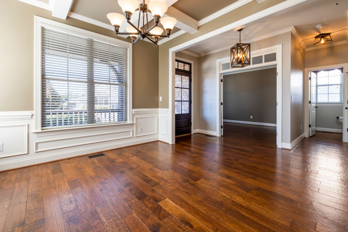 A spacious, well-lit room featuring hardwood floors, elegant light fixtures, and large windows with blinds. Cozy and inviting ambiance.