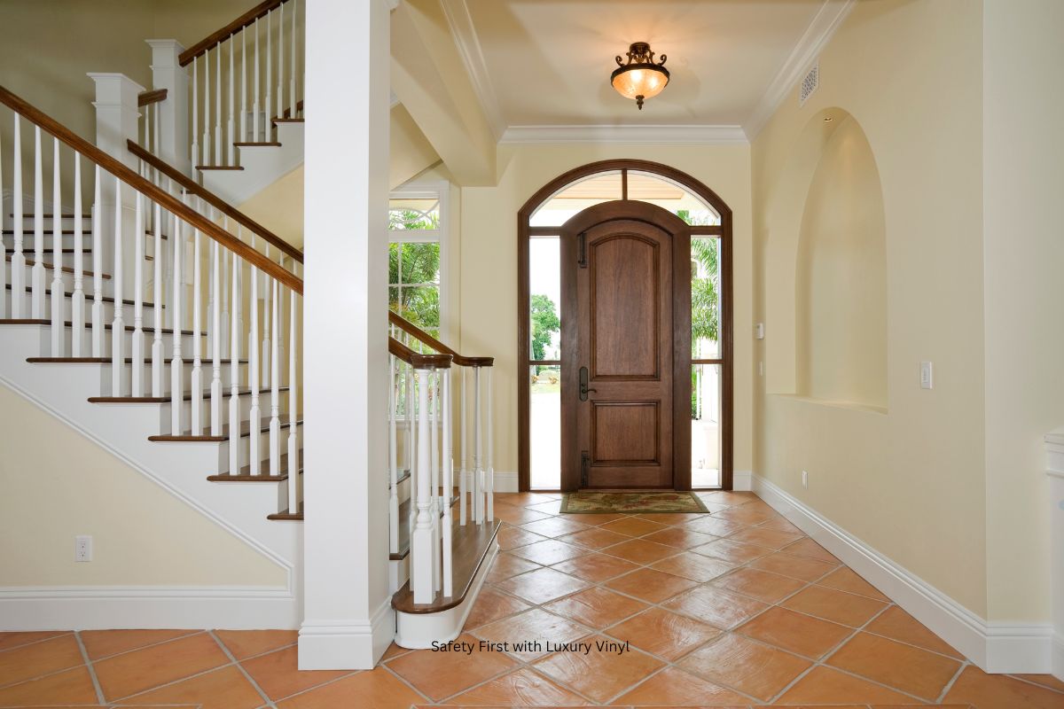 Spacious foyer with a wooden front door, elegant staircase, and terracotta tile flooring, illuminated by a decorative ceiling light.
